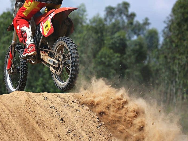 Dirt Bike On a Track With Vibrant Red and Yellow Colors, in the Middle of a Jump With a Cloud of Dust Being Kicked Up By the Rear Tire