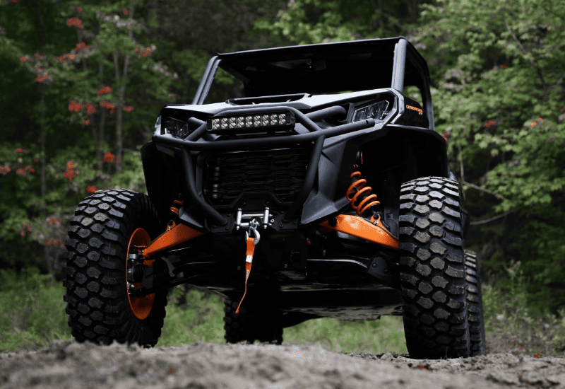 Close-up Frontal View of a Modern UTV With Large, Rugged Off-road Tires, Prominent Orange Suspension Coils, and a Protective Bull Bar With LED Light
