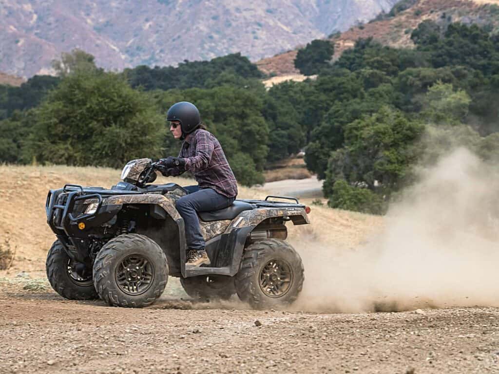 Rider Clad in a Plaid Shirt and Helmet Riding a Honda Fourtrax Foreman Rubicon 4X4 EPS on a Dusty Trail, Kicking up a Trail of Dust Behind them