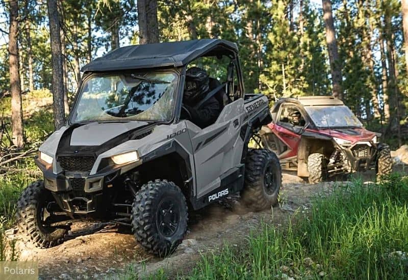 Grey Polaris UTV Navigating Through Rugged Terrain, Behind it, a Red and Black UTV is Also Making its Way Through the Forested Trail