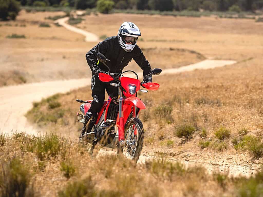 Motorcyclist is Riding a Red Honda CRF450RL Along a Winding Dirt Path Through a Dry, Grassy Field