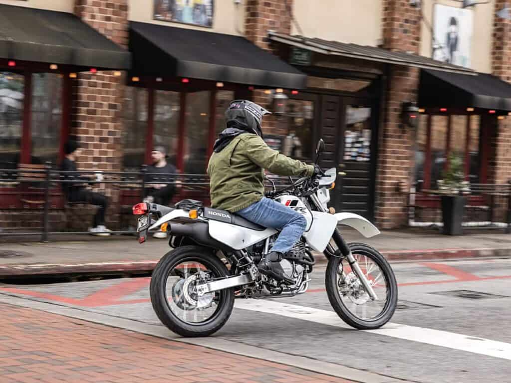 A Rider Dressed Casually on a White Honda Dual Sport Motorcycle Cruising Down an Urban Street 