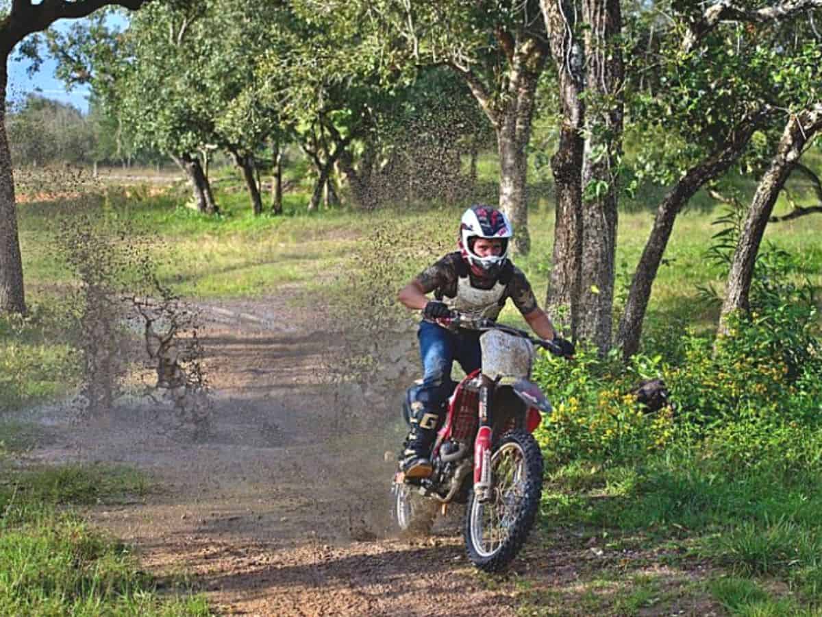 Dirt Biker Wearing a Helmet and Protective Gear Riding Through a Countryside Trail, Kicking Up Mud Behind the Bike