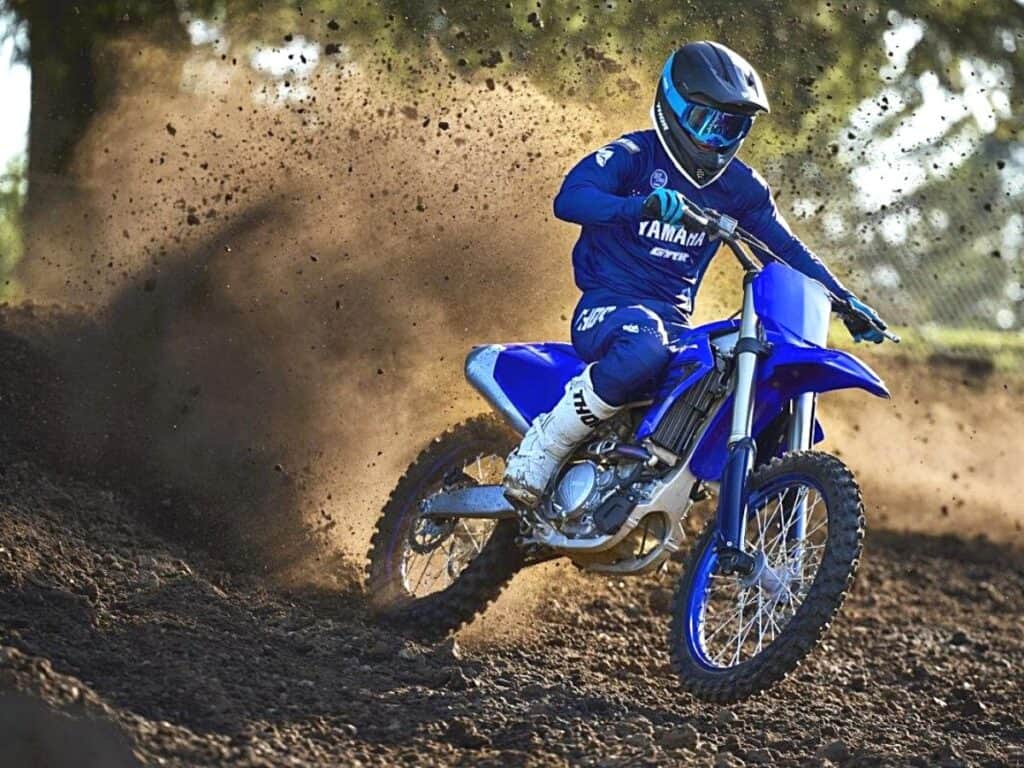 Rider in Full Blue Riding Gear Cornering a Yamaha YZ250F Motocross Bike With a Huge Roost of Dirt and Debris Flying Up Behind the Bike