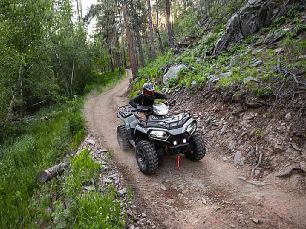 Rider Wearing a Black Helmet With Red Goggles Navigating a Polaris Sportsman 570 ATV on a Narrow Rocky Forest Trail