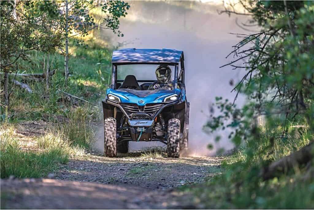 CFMoto ZForce 800 Trail UTV Driving on a Dirt Path Through a Wooded Area, Stirring Up a Cloud of Dust Behind it