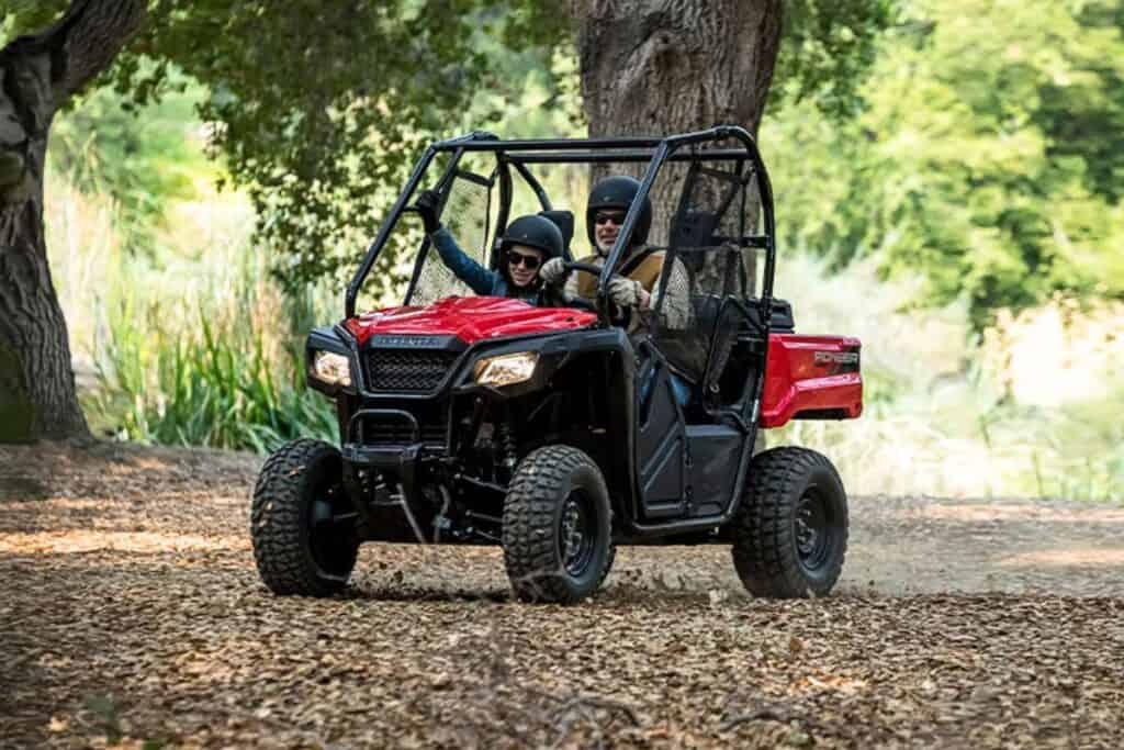 Two people wearing helmets are joyfully riding through a wooded trail in a red Honda Pioneer 520 UTV.