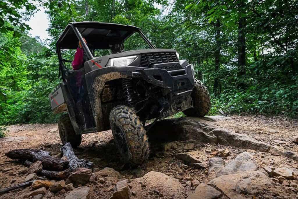 A Polaris Ranger SP 570 UTV is navigating a rocky trail in a lush forest setting.