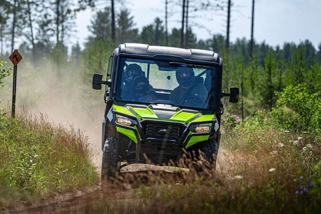 Two people are riding in a lime green Arctic Cat Prowler Pro EPS UTV on a forest trail with a dust trail behind them.