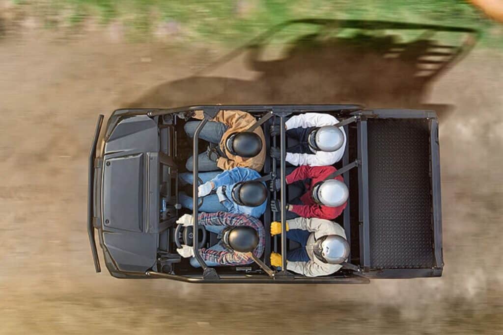 Top-down view of a Kawasaki Mule PRO-FXT UTV with six passengers wearing helmets, driving down a dirt road.