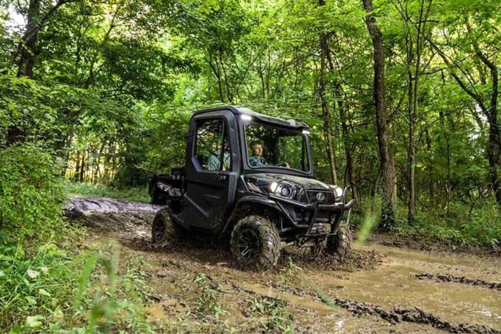 A Kubota Sidekick RTV-XG850 UTV is being driven through a muddy forest trail, showcasing its off-road capabilities.