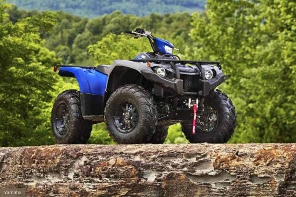 A Yamaha Kodiak 450 ATV perched on a rock ledge against a backdrop of lush greenery.