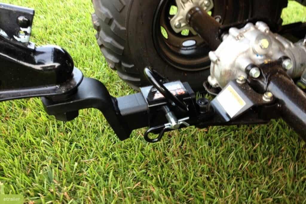 Close-up of an ATV's hitch assembly and rear wheel hub on a grassy surface.