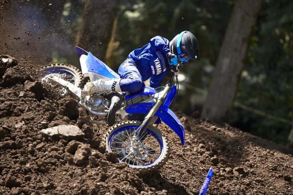 Close-up side view of a blue Yamaha YZ125 dirt bike kicking up dirt on a motocross track in the woods.