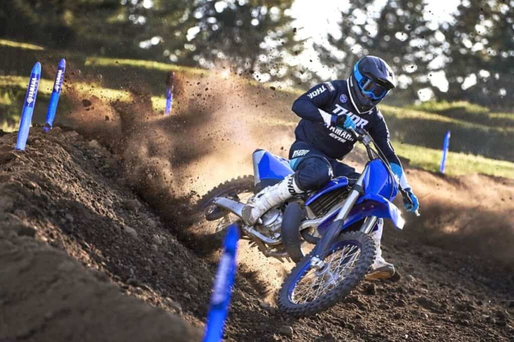 A rider clad in blue gear aggressively corners the Yamaha YZ250, throwing up a spray of dirt on the track.