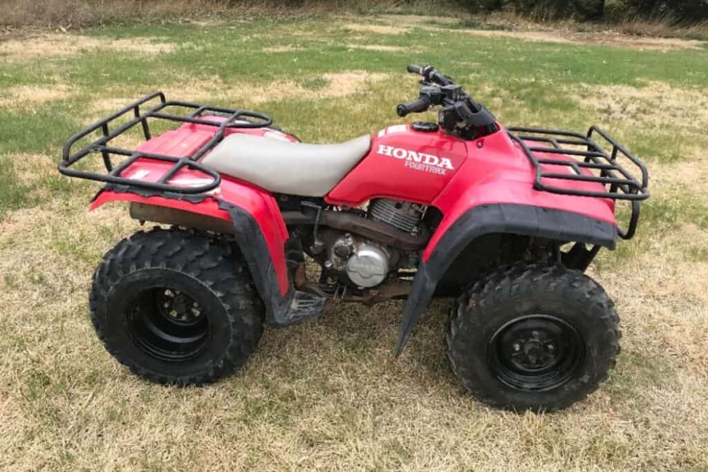 Side view of the Honda Fourtrax 300 parked in a field.