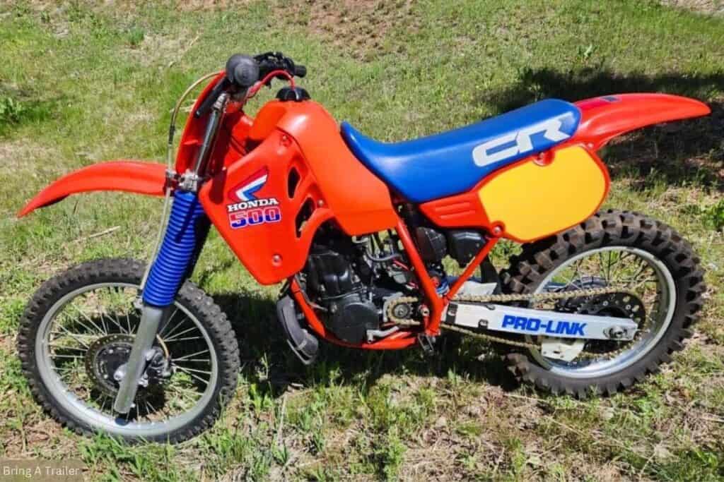 A red and blue Honda CR 500 dirt bike parked on grass.