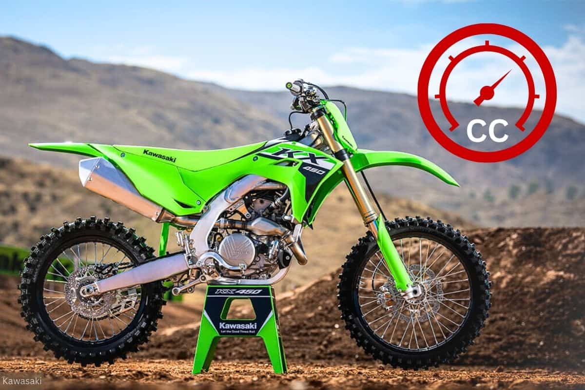 A green Kawasaki KX450 dirt bike on a stand outdoors with a mountainous landscape in the background, and a red gauge in the upper right corner indicating engine displacement size.