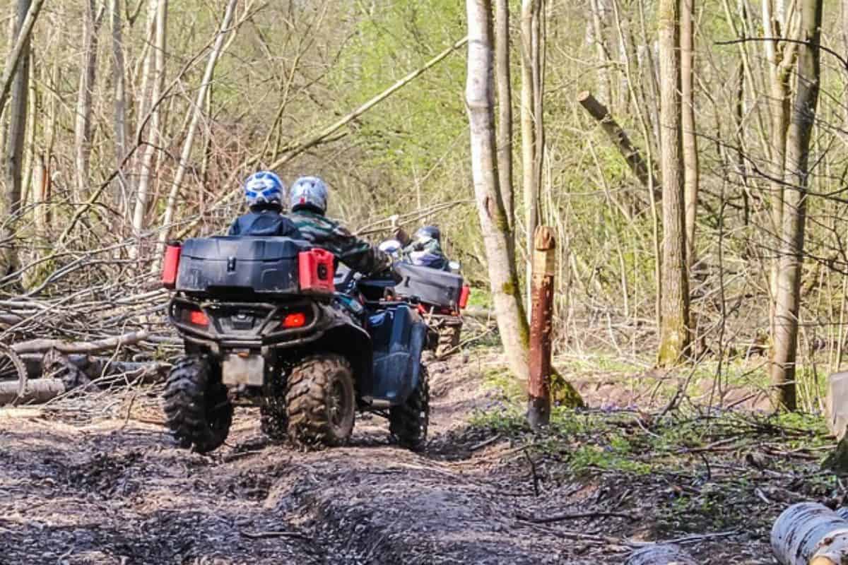 Two hunters riding the best atv for hunting on a muddy forest trail.