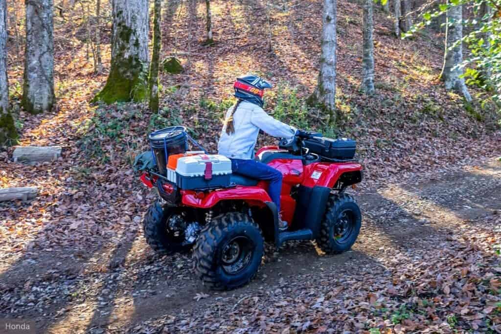 A rider on a Honda FourTrax Rancher, navigating a leaf-covered forest trail.